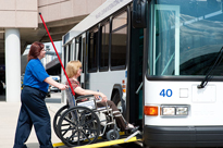 Airport staff assisting woman in wheelchair onto bus